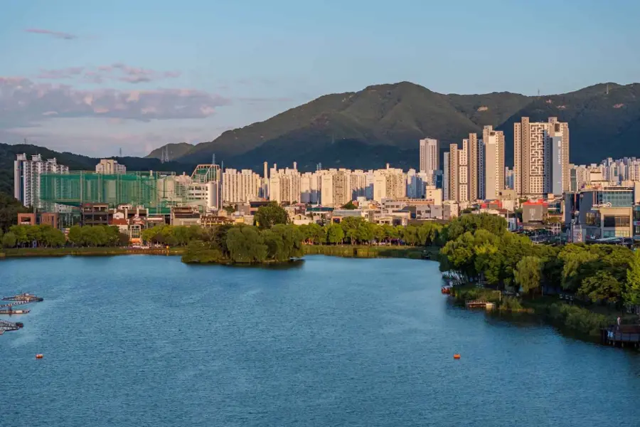 Suseongmot Lake before sunset with its small island, distant hills and Daegu apartment skyline