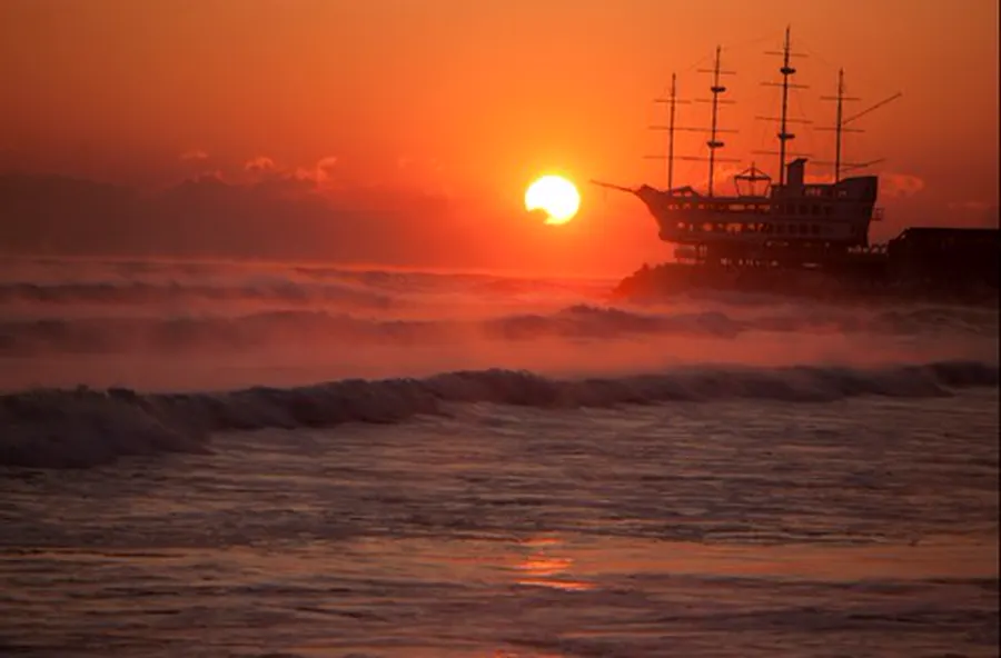 Sunrise over waves at Jeongdongjin with a ship-shaped building in silhouette